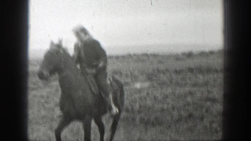 A horseback rider appears closer to the camera in an open Montana field, with soft black-and-white 8mm detail.