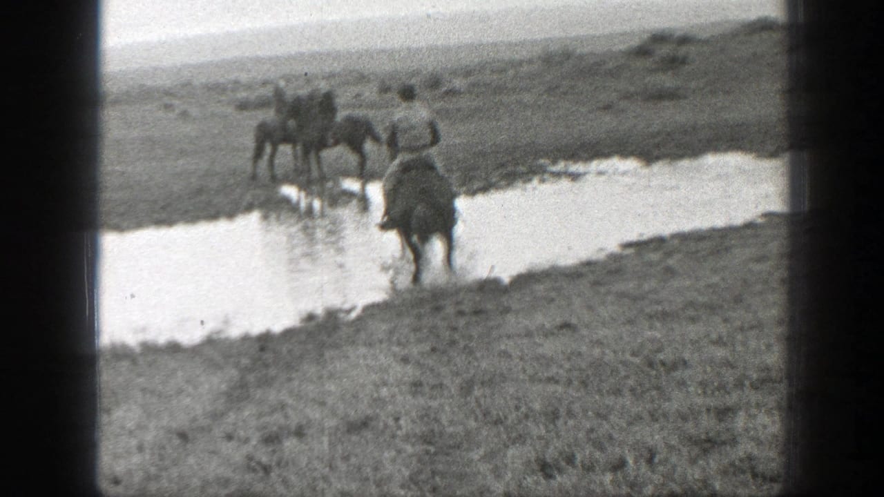 Men on horseback appear to cross a shallow stream in Montana grassland, filmed in soft 8mm black-and-white footage.