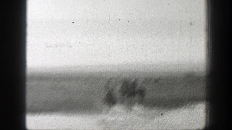 A soft 8mm frame shows riders and horses as blurred shapes moving near shallow water in open Montana range country.