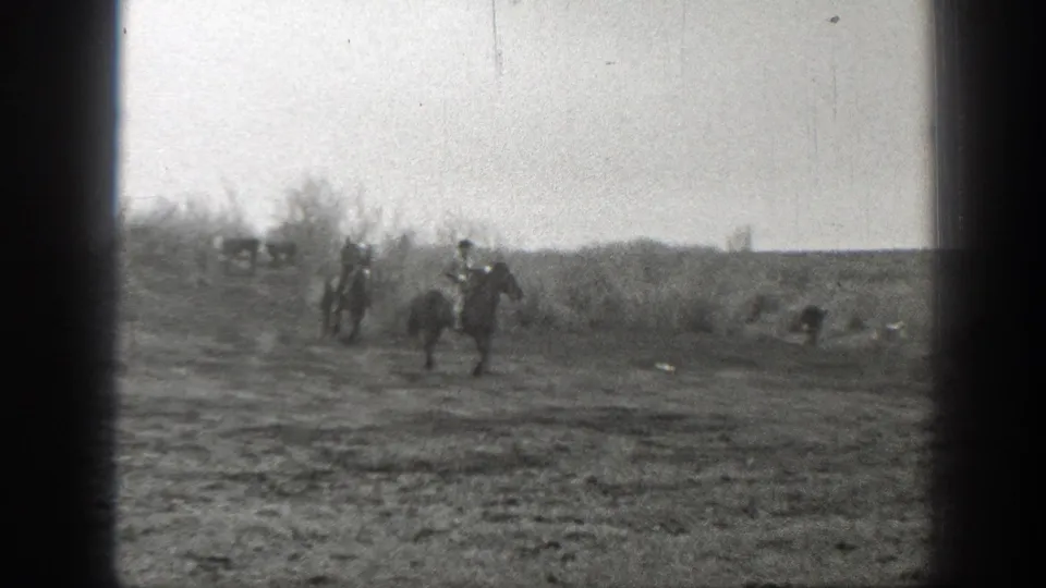 Riders on horseback travel across a rough Montana field while cattle remain near the brush in this 1939 home-movie frame.