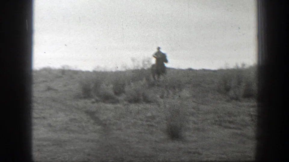 A distant horseback rider crosses rough Montana rangeland in soft black-and-white 8mm footage.