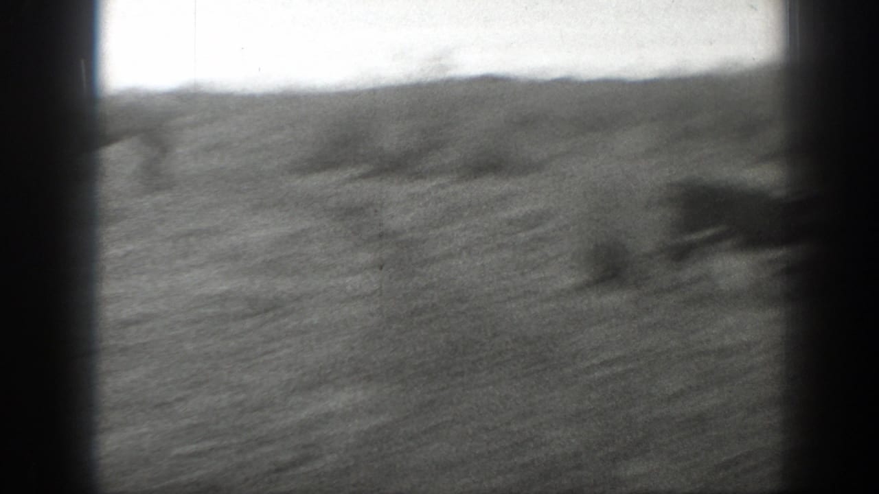 Soft black-and-white 8mm view of an open Montana field with low hills and heavy frame-edge vignetting.