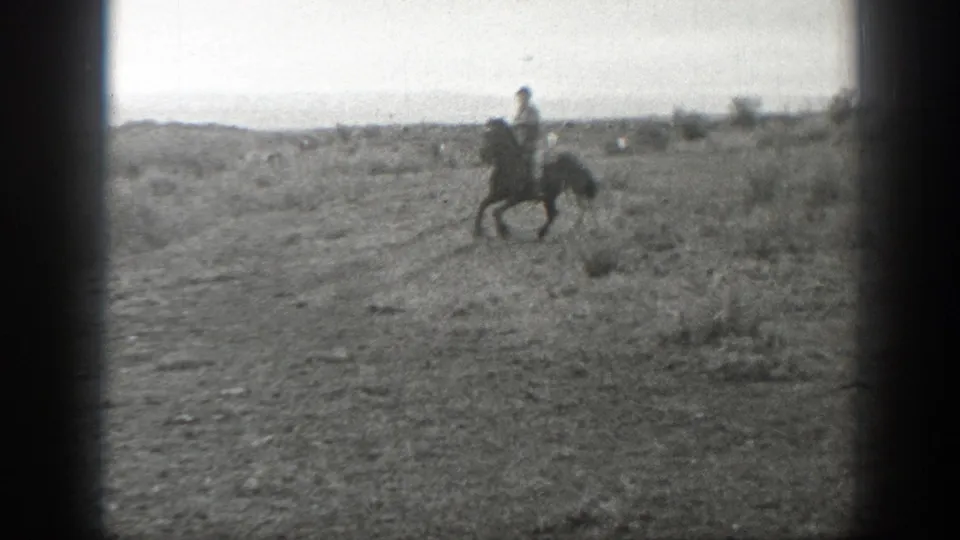 Distant horseback rider crosses an open Montana pasture in grainy black-and-white 8mm footage.