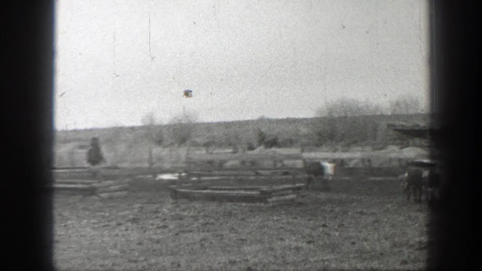 Black-and-white 1939 Montana frame with cattle spread across pasture, low fence rails, and a distant figure on horseback.