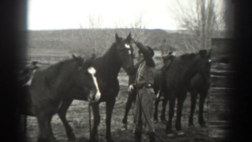 A man in ranch clothing stands among horses in 1939 Montana footage, with open land and bare trees behind the group.
