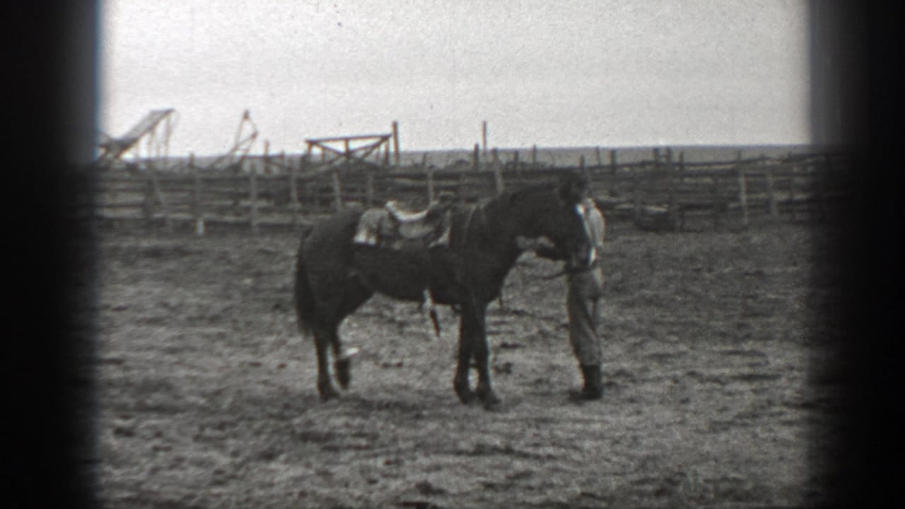 Man stands beside a saddled horse near wooden corral fencing.
