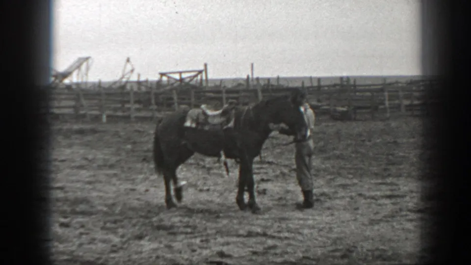 The man stands close to the saddled horse in the Montana corral, with wooden fencing and ranch equipment visible behind them.