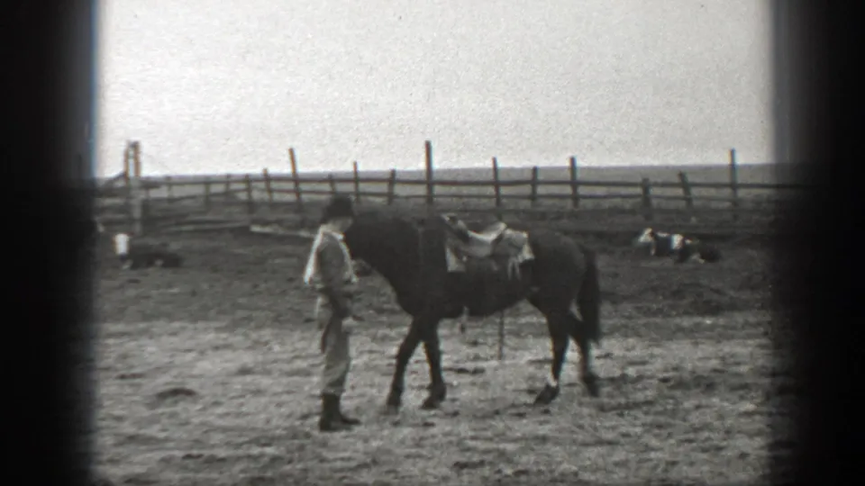 1939 Montana frame showing a person beside a saddled horse in a dirt ranch enclosure, with cattle resting along the fence line.