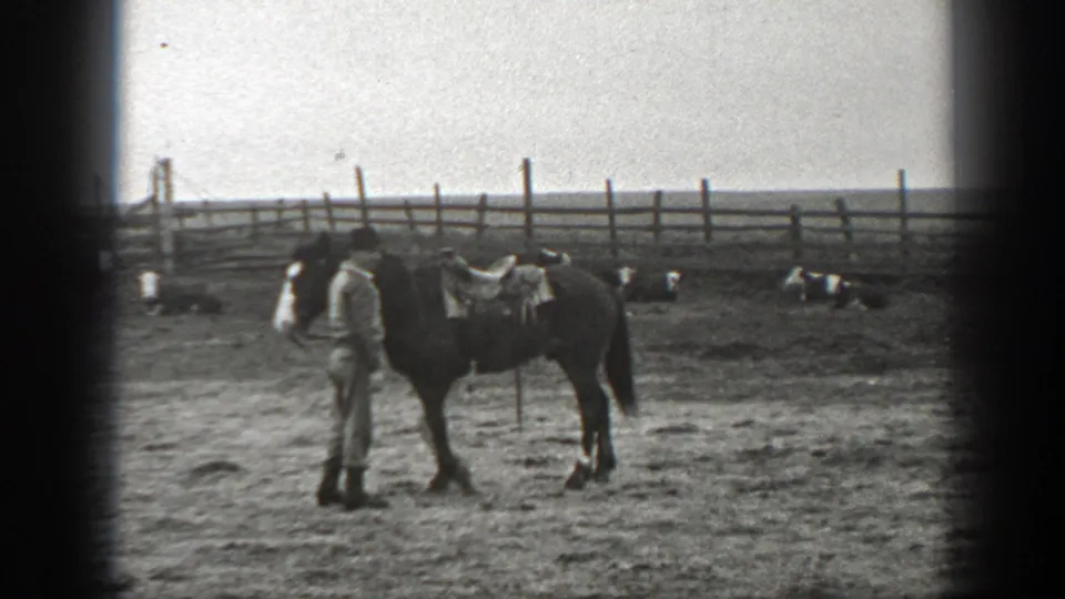 A person faces a saddled horse in a fenced Montana ranch corral, seen in grainy 1939 8mm home-movie footage.