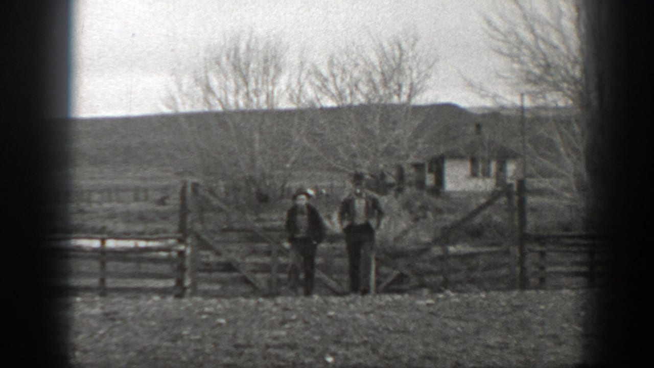 Two people stand by a ranch gate while a third figure or horse appears near the fence line.
