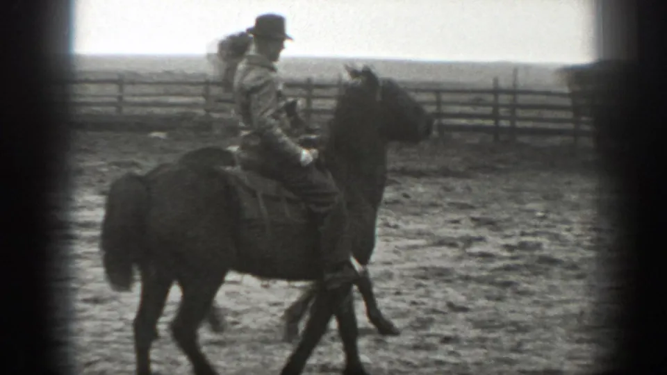 Mounted adult man in a hat and jacket rides past a rail fence in rural Montana, 1939.