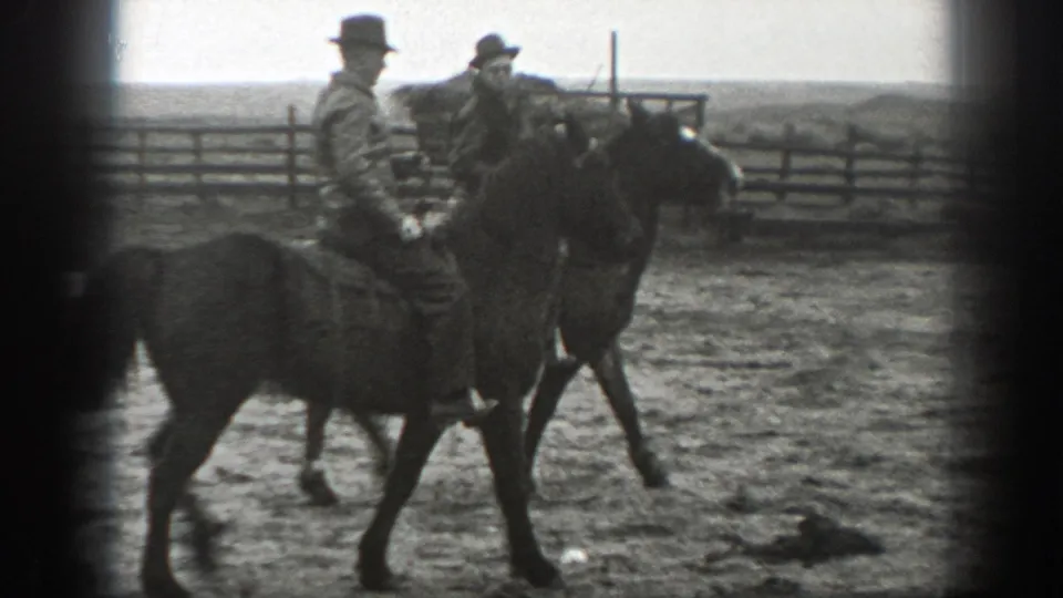 Two adult riders on saddled horses move through a dusty Montana enclosure in 1939 home-movie footage.
