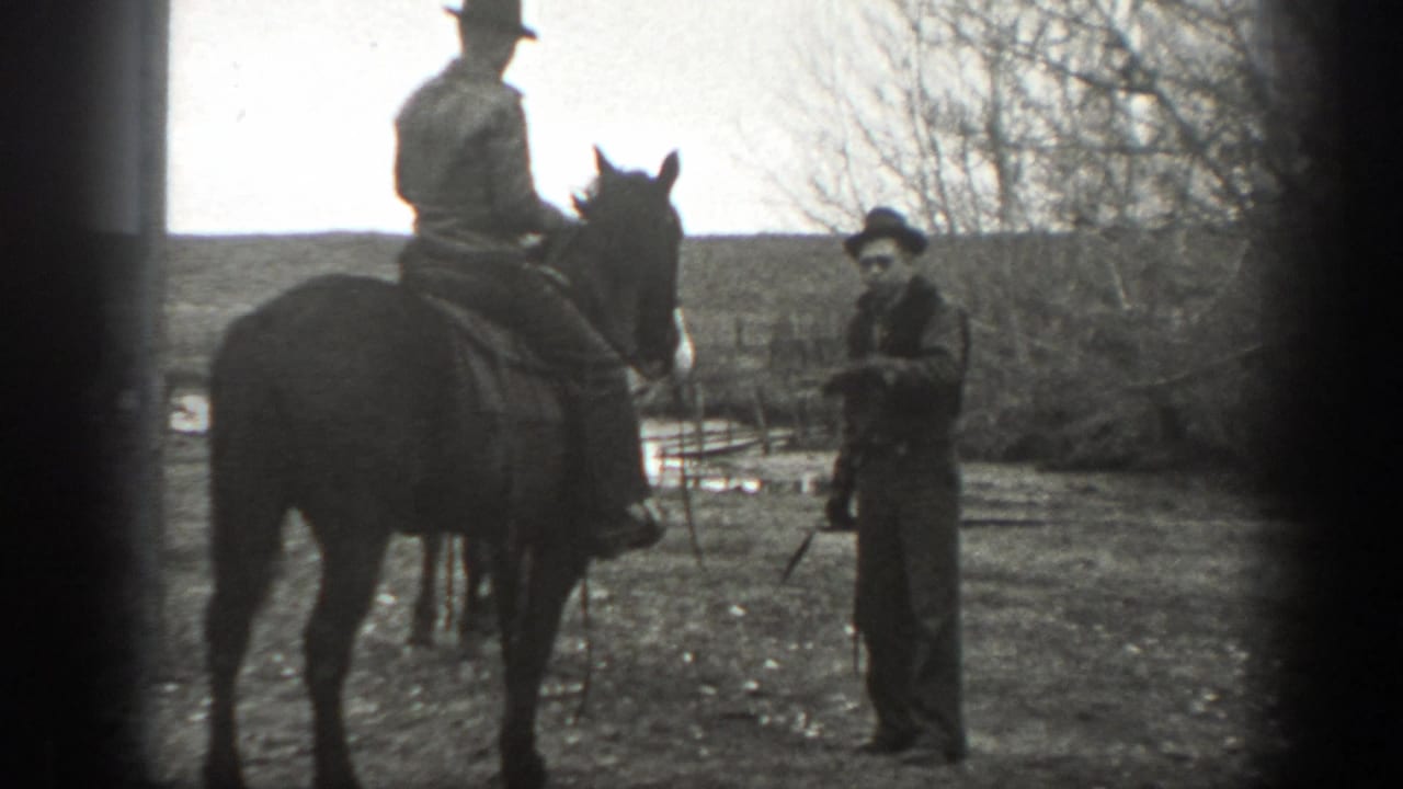 A mounted rider pauses near another adult man standing by sparse trees in rural Montana, 1939.