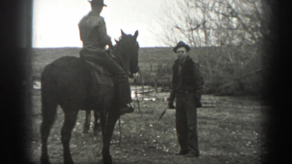 1939 Montana 8mm frame showing a mounted man and a standing man in dark clothing in an open ranch field.