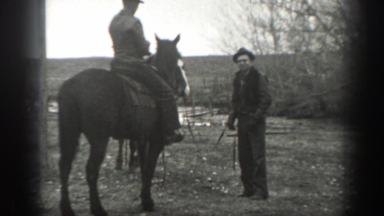 1939 Montana ranch scene with a standing man in a dark hat near a saddled horse and rider, framed by bare trees and pasture.