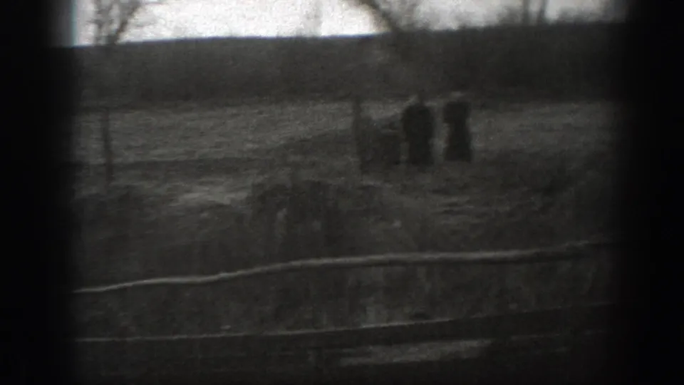 Grainy 1939 Montana 8mm frame of a fenced pasture with distant cattle forms, open grass, and a dark tree line beyond.