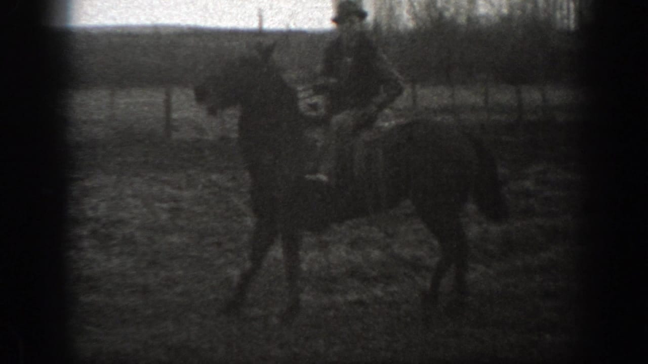 Grainy 1939 Montana 8mm frame with a man riding a horse across open rural ground beside fencing.