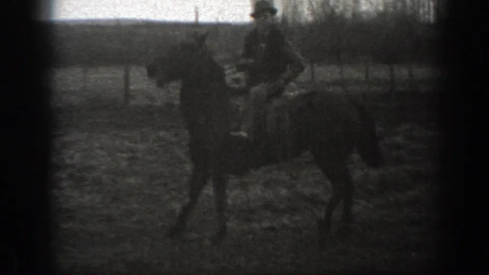 Grainy 1939 Montana 8mm frame with a man riding a horse across open rural ground beside fencing.