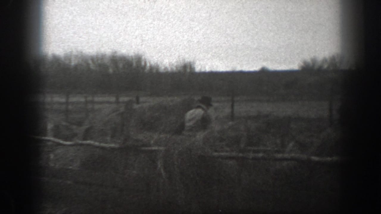 Grainy 1939 Montana 8mm frame showing a person working or moving near rough fencing in an open field.