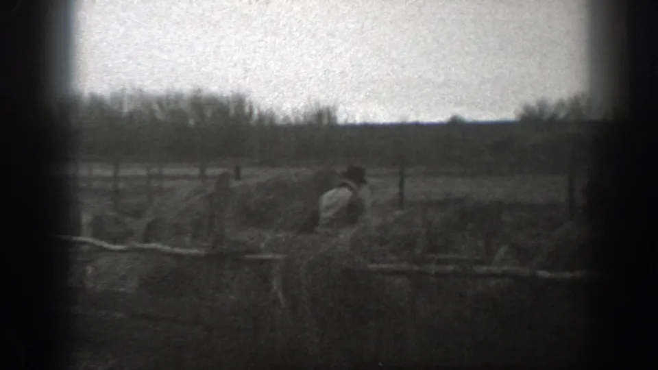 Grainy 1939 Montana 8mm frame showing a person working or moving near rough fencing in an open field.