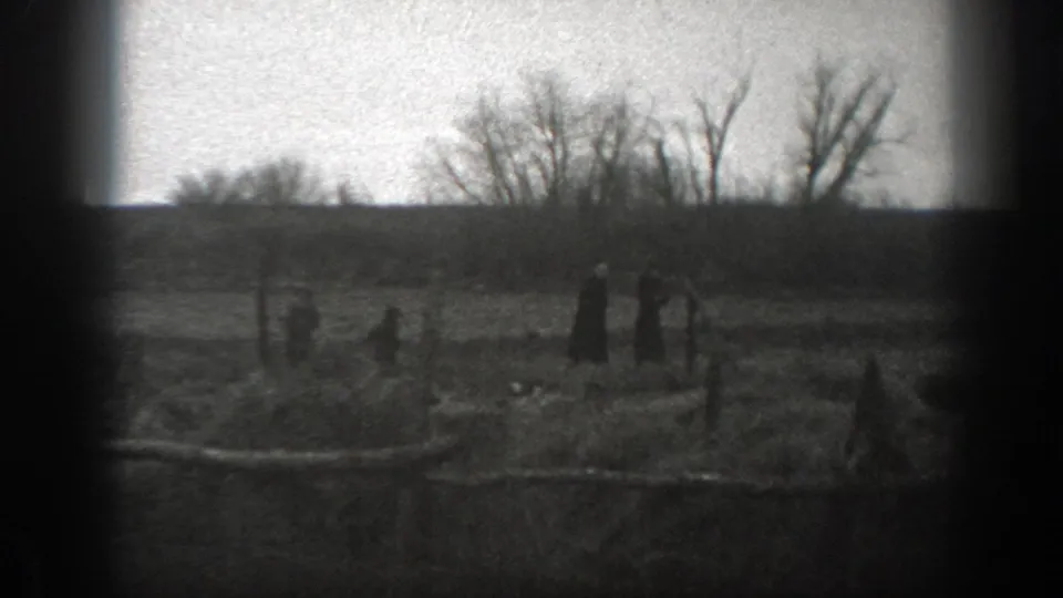 In a 1939 Montana farm scene, distant family members walk through a fenced pasture with bare trees and open ground behind them.