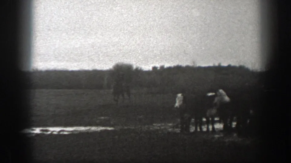 1939 Montana 8mm frame showing distant people gathered near horses or a wagon in an open field with a treeline beyond.