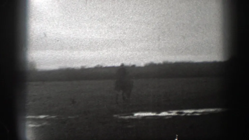1939 Montana 8mm frame showing a soft, distant rider on horseback crossing a broad field with low hills or treeline in the background.