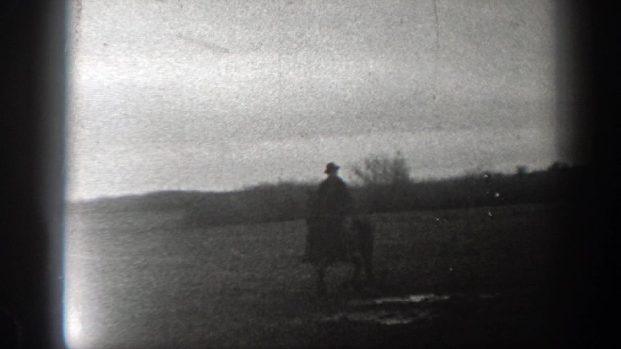 Lone rider on horseback crossing an open field under a hazy sky.