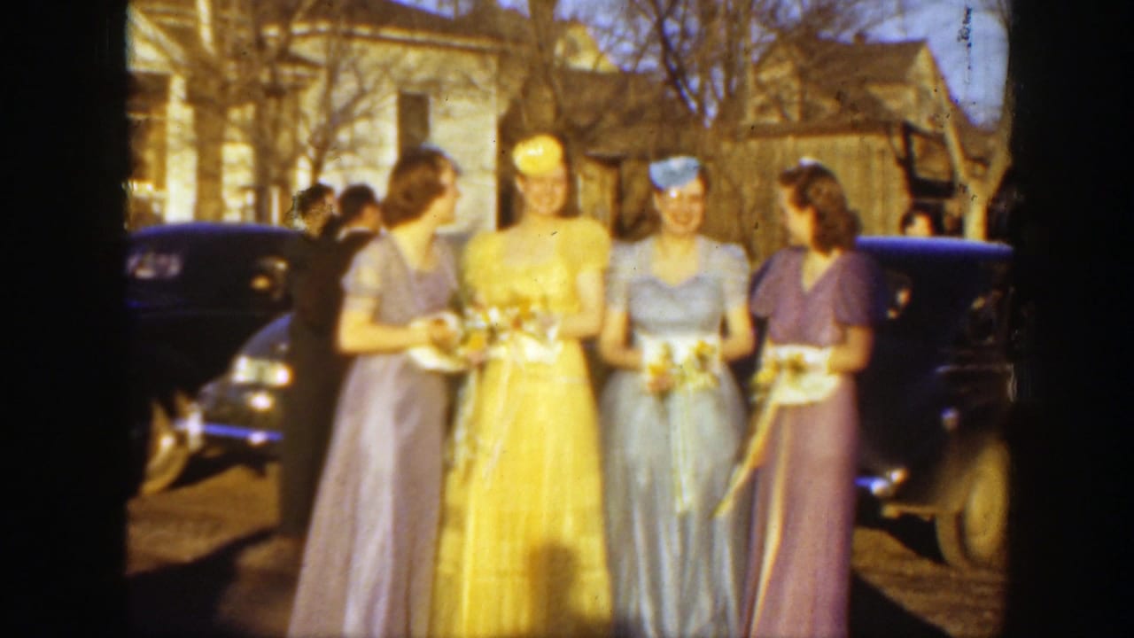 Four young women in 1930s-style formal dresses stand outdoors with bouquets near a dark automobile in Montana footage.