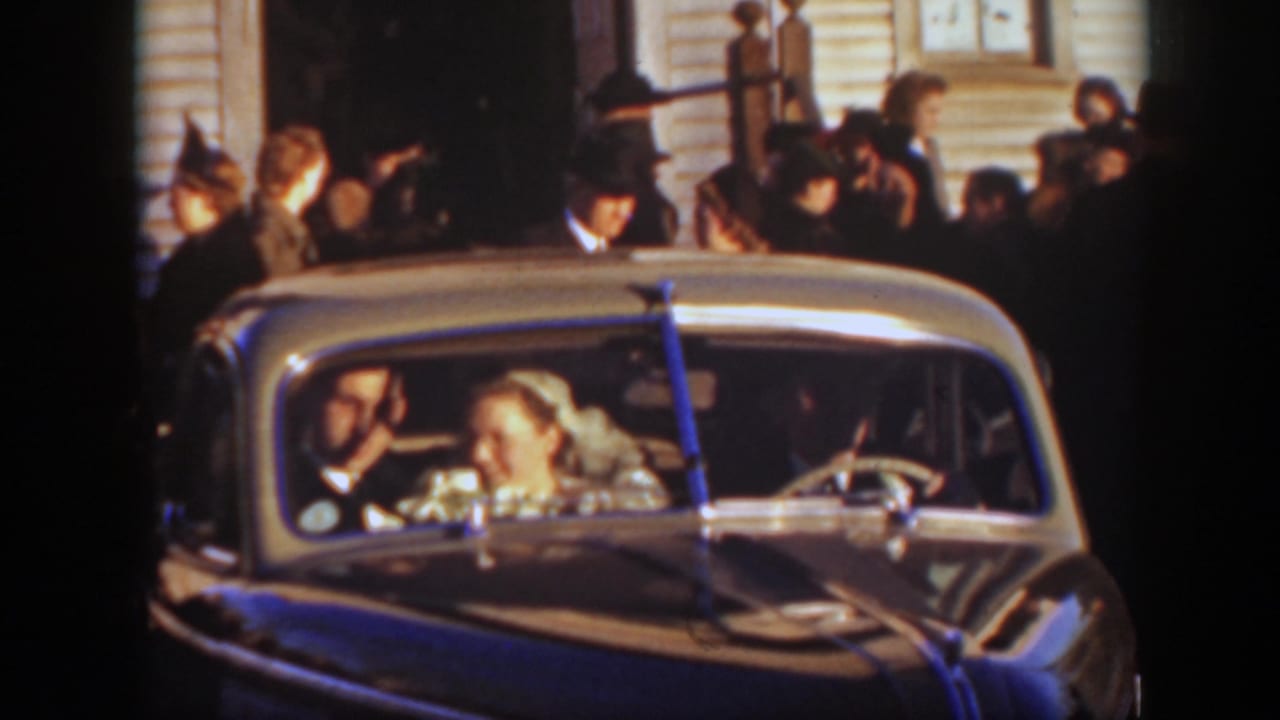 The bride and groom smile inside a ribboned car as guests crowd around the church exterior in 1939 Montana footage.