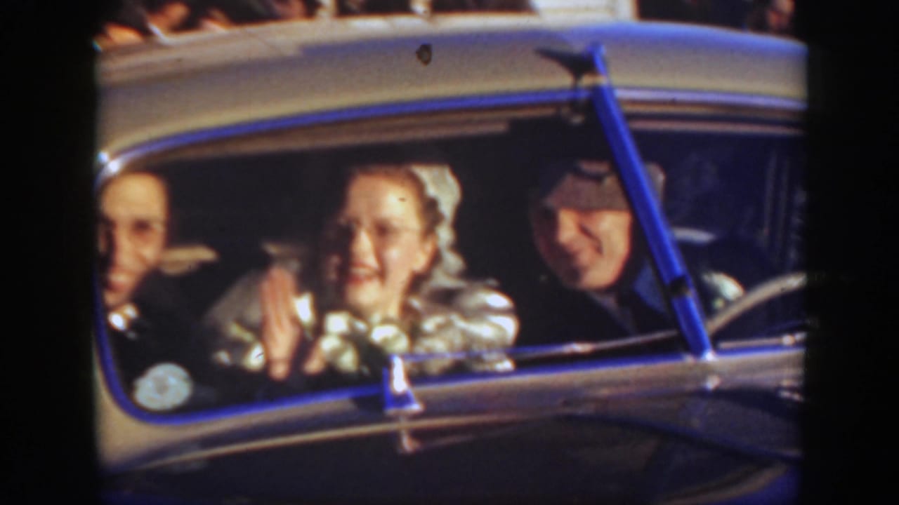 1939 Montana wedding frame with the bride smiling from a vintage car, flanked by male passengers and watched by people outside.