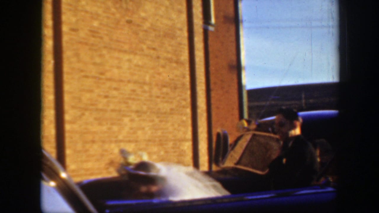 1939 Montana wedding footage shows the car near a brick building, likely at the church-side arrival area described in the clip metadata.