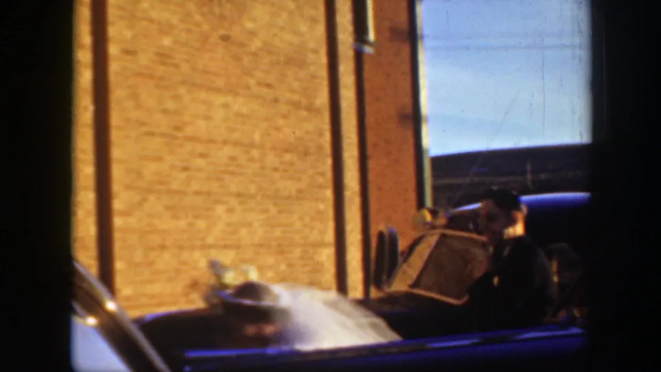 1939 Montana wedding footage shows the car near a brick building, likely at the church-side arrival area described in the clip metadata.