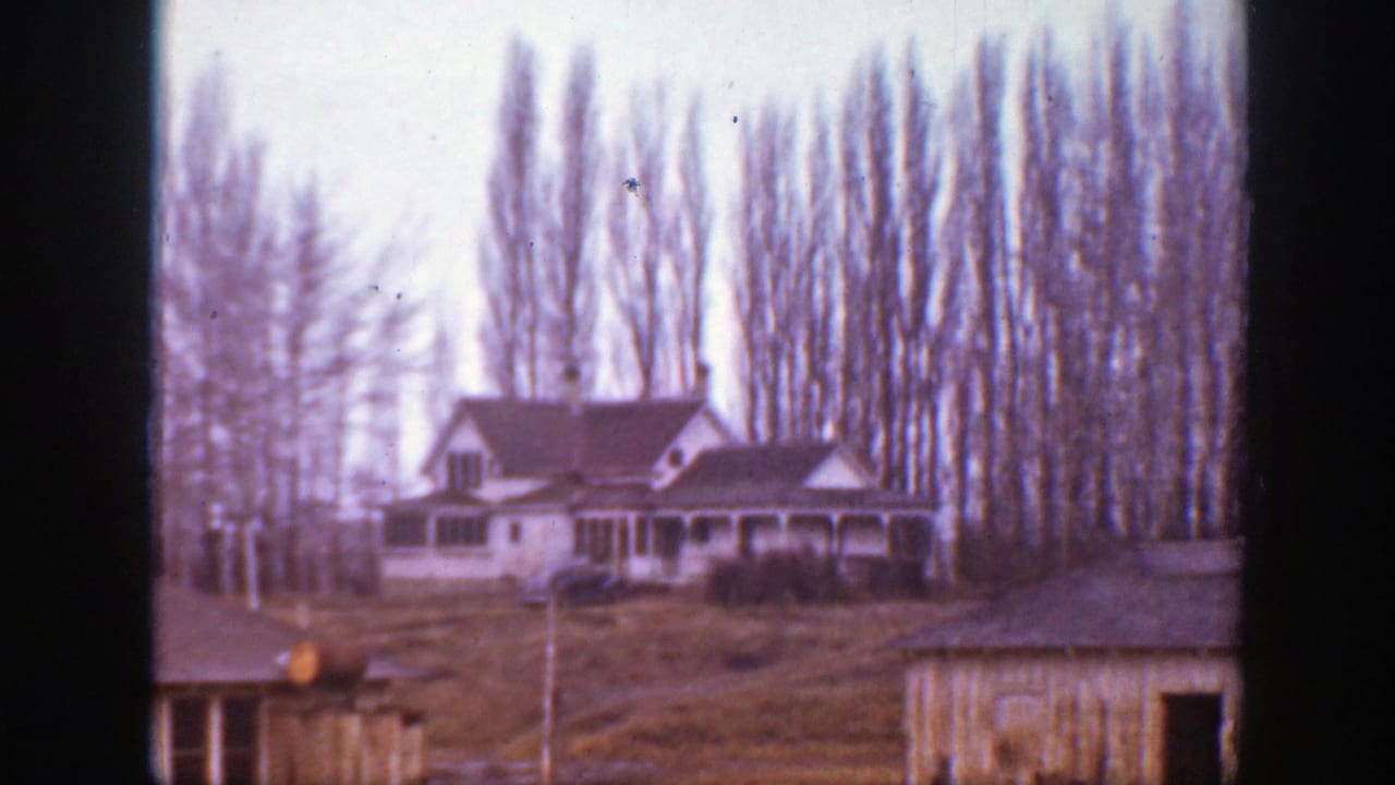 1939 Montana home-movie frame showing a house, open yard, small outbuilding, and tall leafless trees in soft focus.