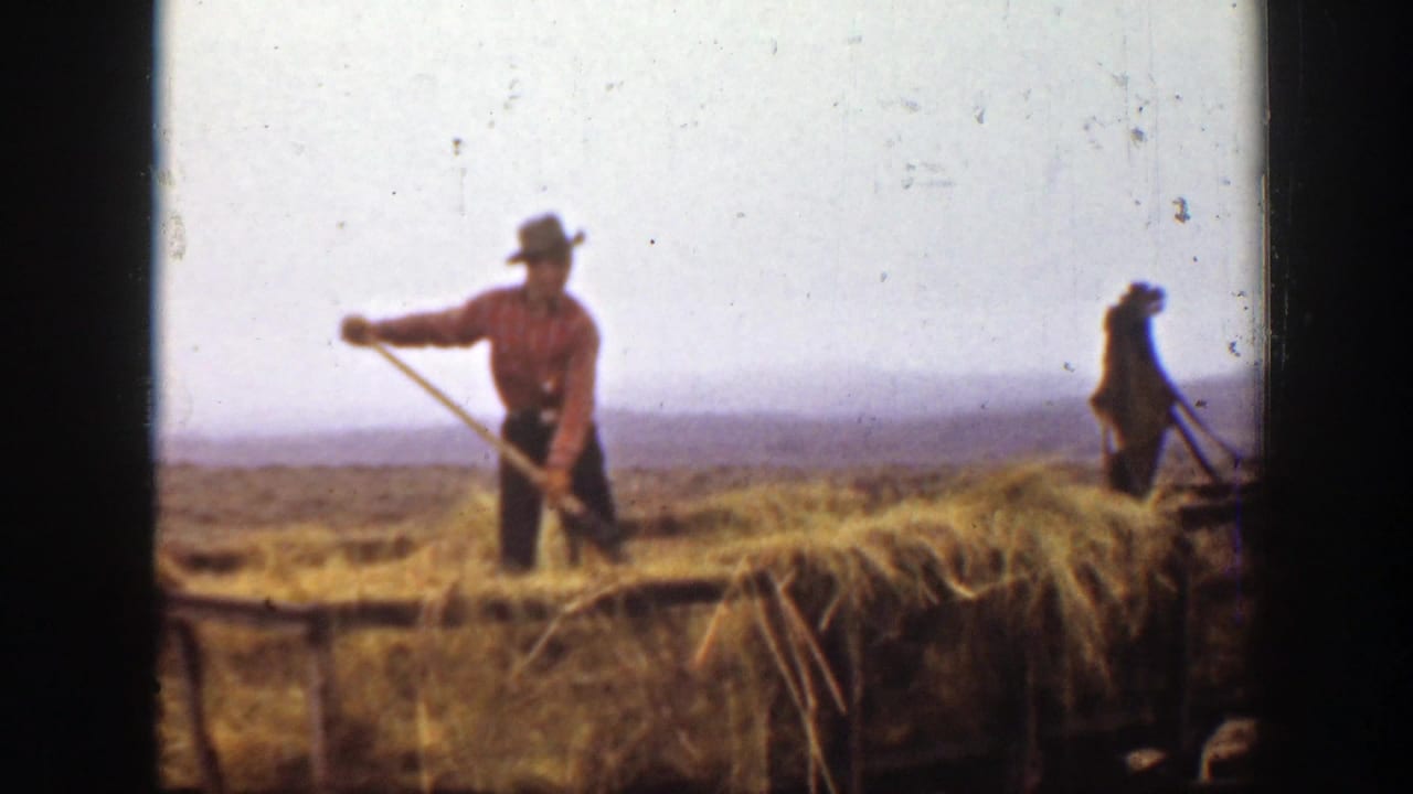 1939 Montana 8mm frame of a farm worker standing in straw with a pitchfork, with a second worker visible in the background.
