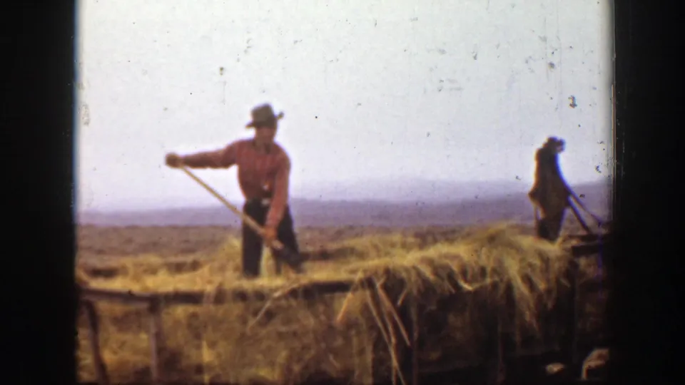 1939 Montana 8mm frame of a farm worker standing in straw with a pitchfork, with a second worker visible in the background.