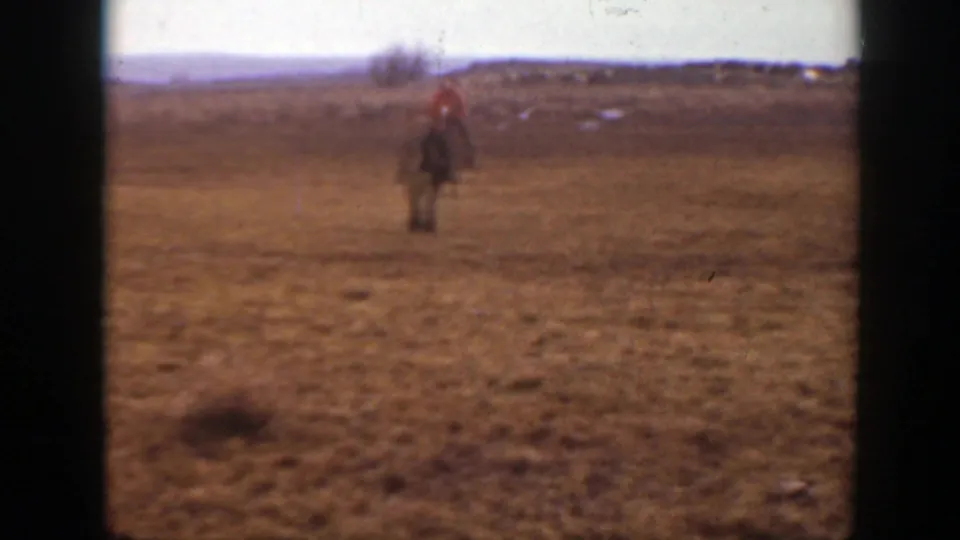 A child in a bright red jacket appears to ride a horse toward the camera across a broad Montana field.