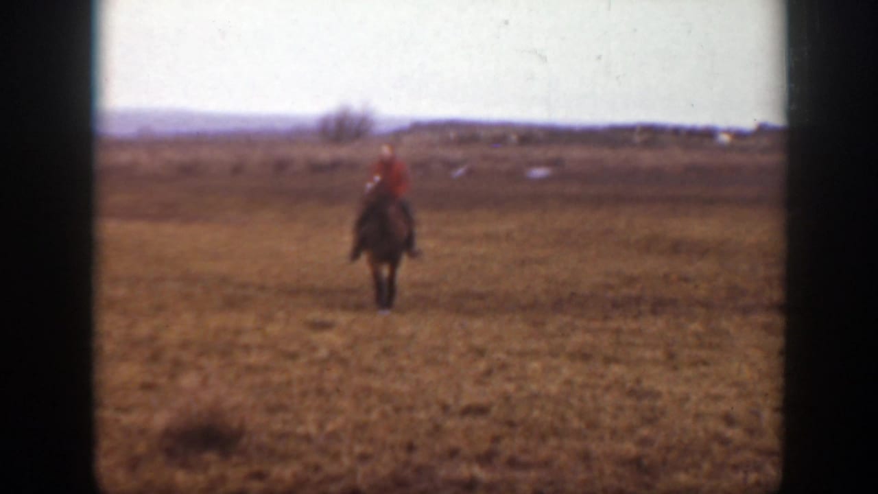 The mounted child is closer to the camera, framed against dry Montana grassland and a low, open horizon.