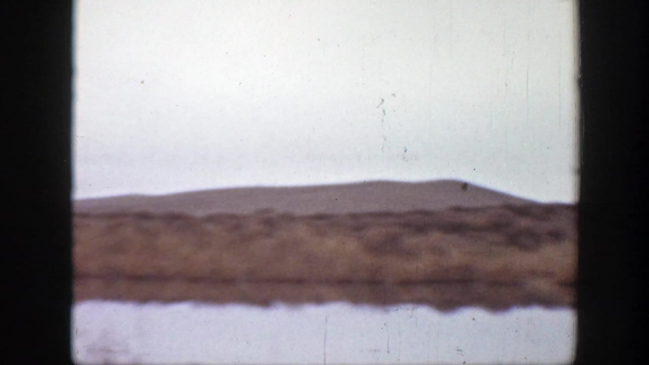 1939 Montana home-movie frame showing open plains, low hills, and a pale sky with no riders visible in this moment.