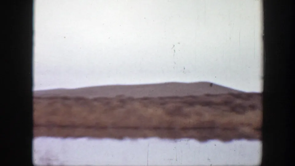 1939 Montana home-movie frame showing open plains, low hills, and a pale sky with no riders visible in this moment.