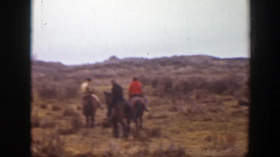Three horseback riders cross the Montana plains in a distant 1939 home-movie view, with low hills and dry grassland around them.