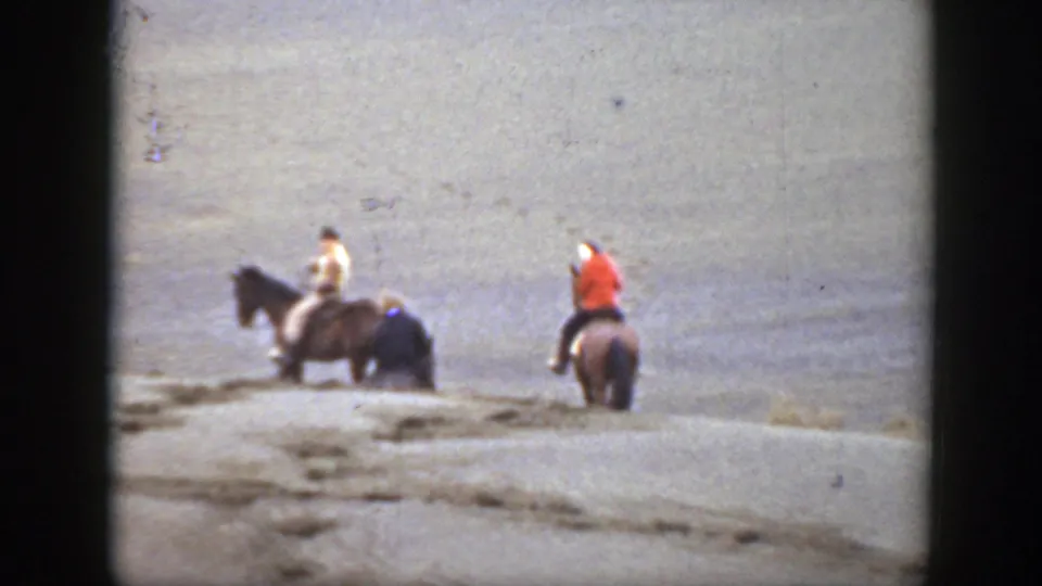 A late-1930s Montana home-movie frame shows three men on horseback crossing a sparse arid slope.