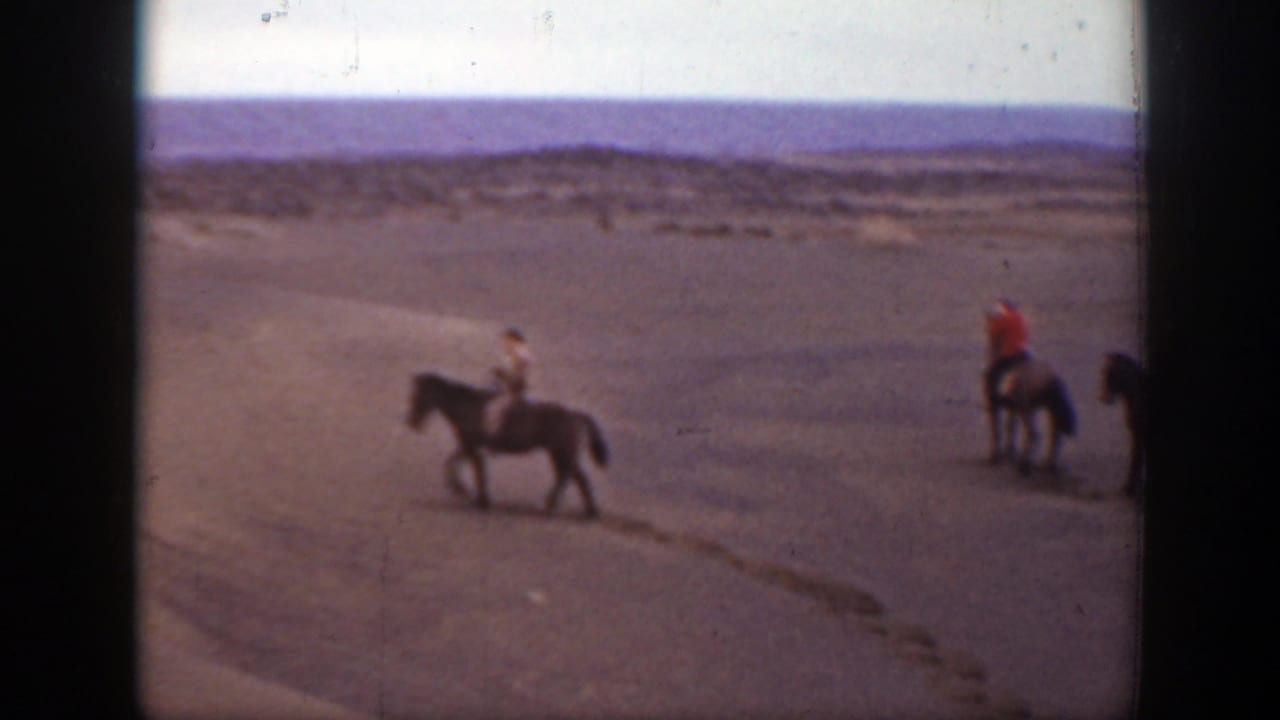 1939 Montana 8mm frame showing horseback riders crossing a sandy open landscape with distant low hills and black film borders.