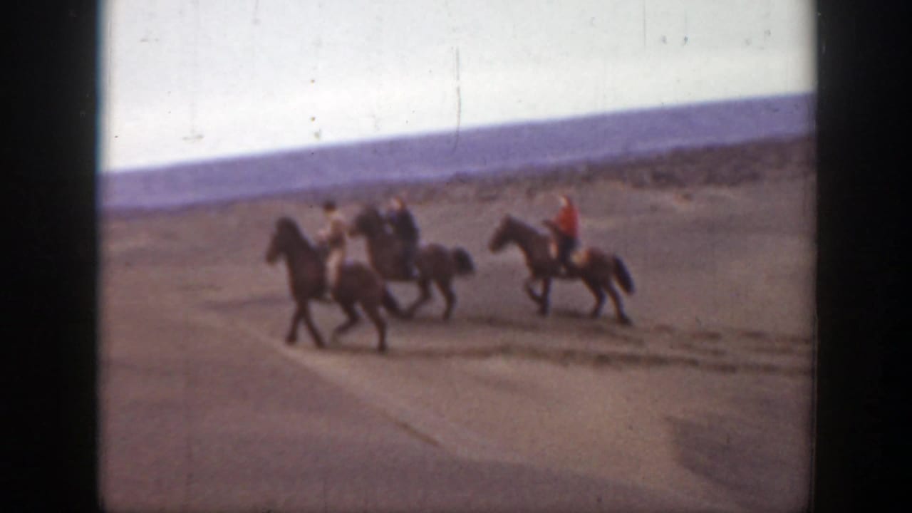 Three riders continue across open sand, with one rider wearing a red top.