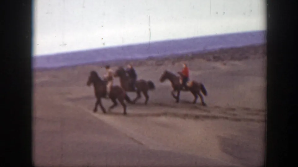 Horseback riders pass through a broad sandy area, including one rider in red, in the 1939 Montana home-movie clip.