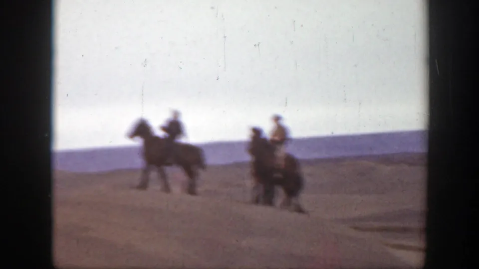 The riders move farther across the sandy landscape, with soft 8mm focus and motion blur obscuring facial detail.