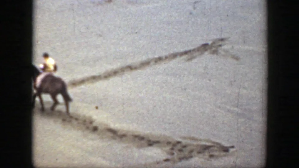 A single rider on horseback crosses pale sand, following visible tracks in the Montana 1939 home-movie footage.
