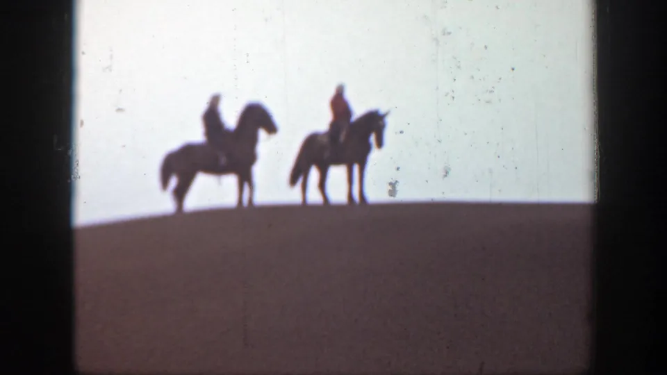 The final 8mm frame shows two mounted riders in silhouette on a sloping Montana ridge, with sky and film grain visible.
