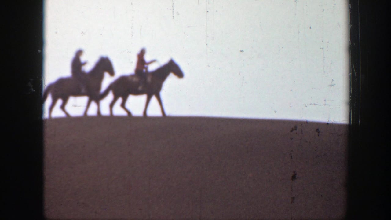Two horseback riders in silhouette move along a ridge in 1939 Montana home-movie footage, seen against a pale sky.
