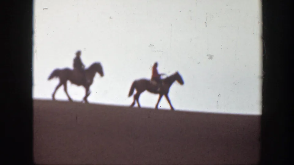 Two distant riders on horseback appear in silhouette across a low Montana ridge in a 1939 8mm frame.